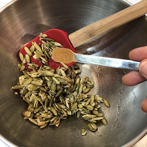 cinnamon in teaspoon over pumpkin seeds in metal bowl