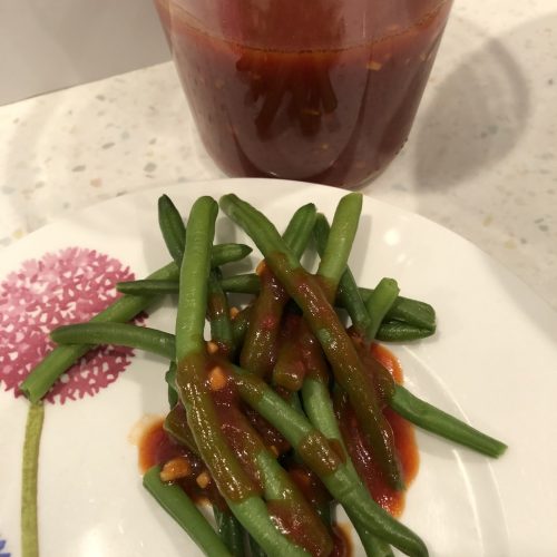 fermented ketchup dressing over green beans with the container of dressing behind the plate with beans