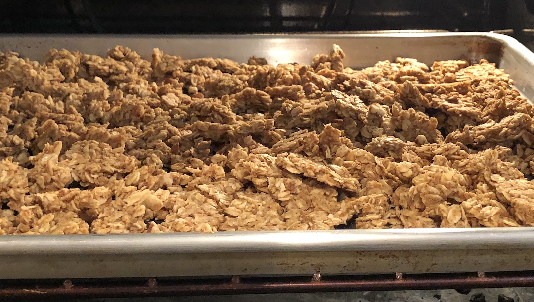 Big chunks of nut free, gluten free granola on a rimmed baking sheet in the oven