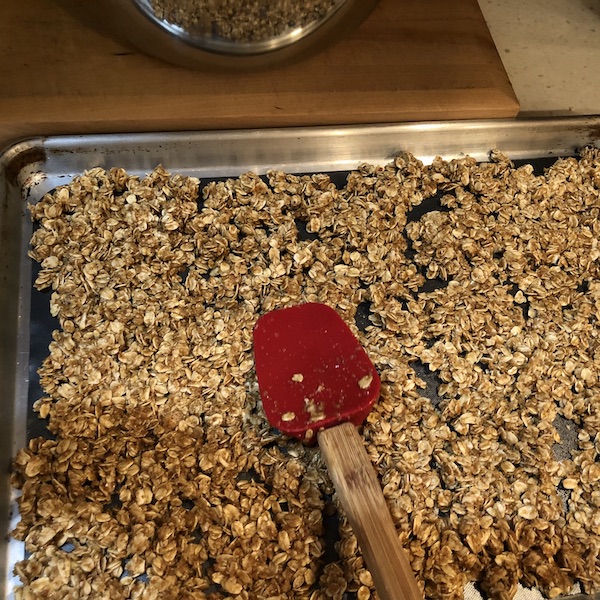 Patting down granola in lined baking pan with a silicone spatula