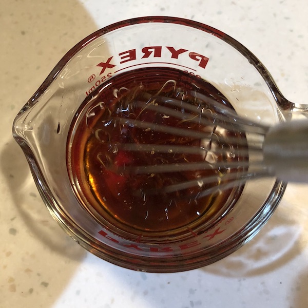whisking maple syrup, oil and water in a glass measuring cup.