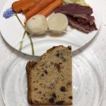 Irish soda bread on a clear plate with corned beef, potatoes, carrots & cabbage in the background
