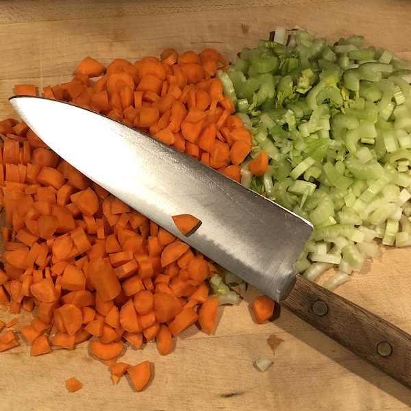chopped carrots & celery on cutting board with cooks knife on top