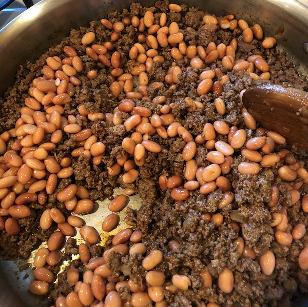 Stirring in pinto beans to browned meat.