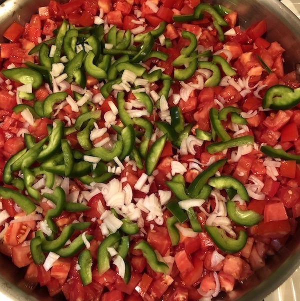 Tomatoes fill pan with fewer shallots & peppers on top.