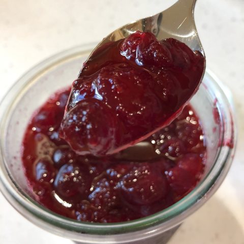 cranberry sauce on a spoon over a glass jar of cranberry sauce