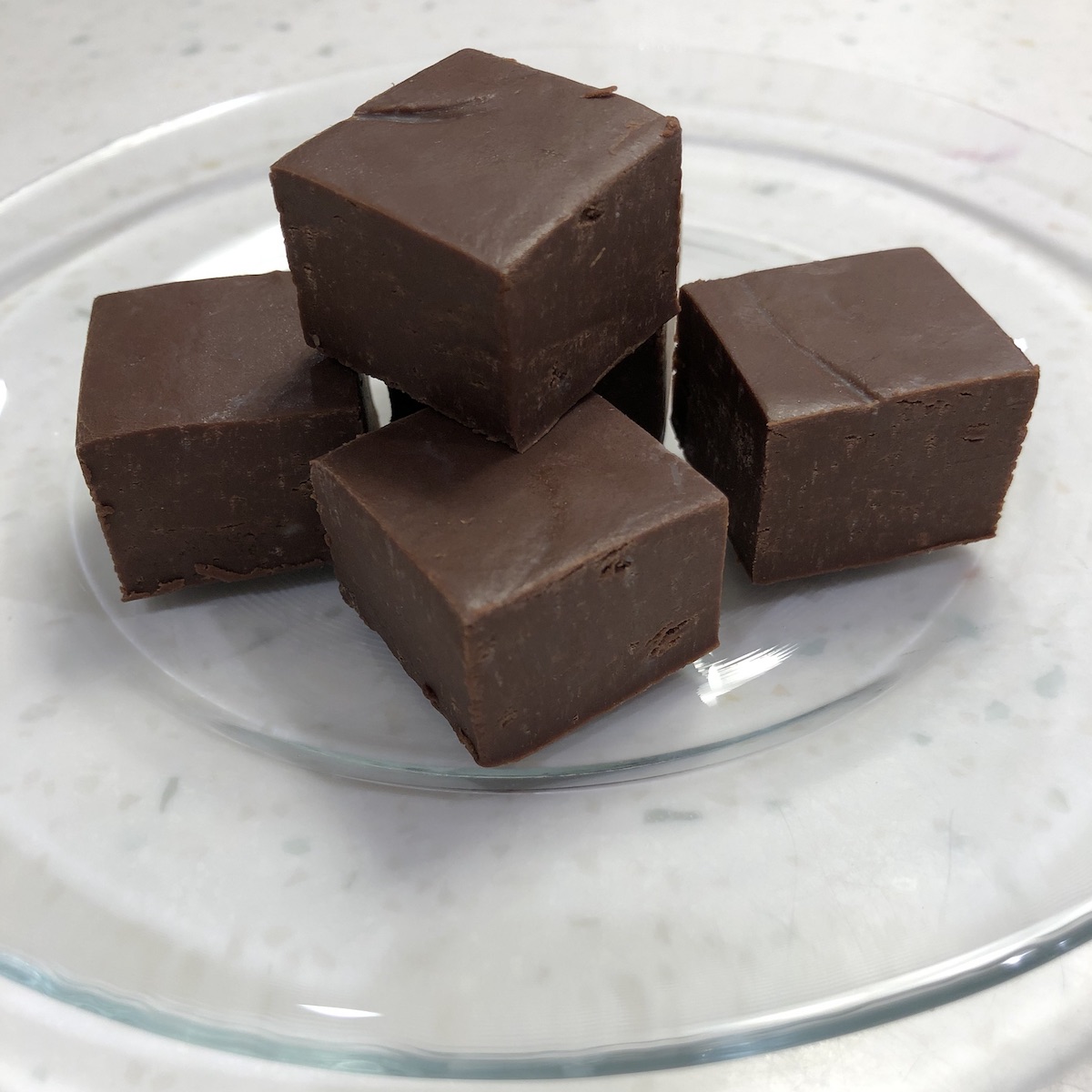 5 pieces fudge sitting on a glass plate on a white speckled counter