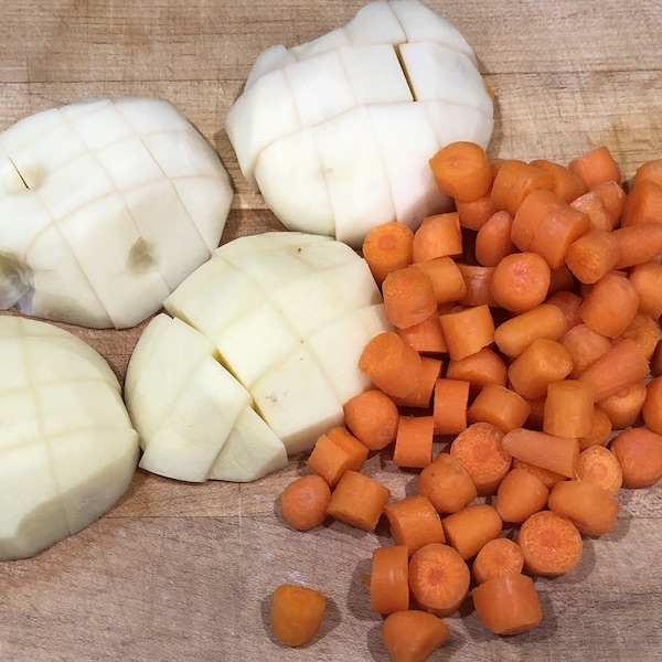 two chopped potatoes and carrots on a wooden cutting board