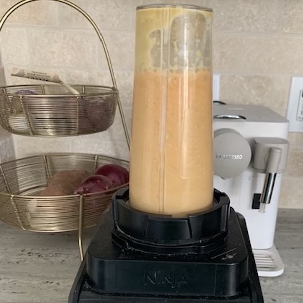 Sauce ingredients being blended in blender with a tall cup and black base.