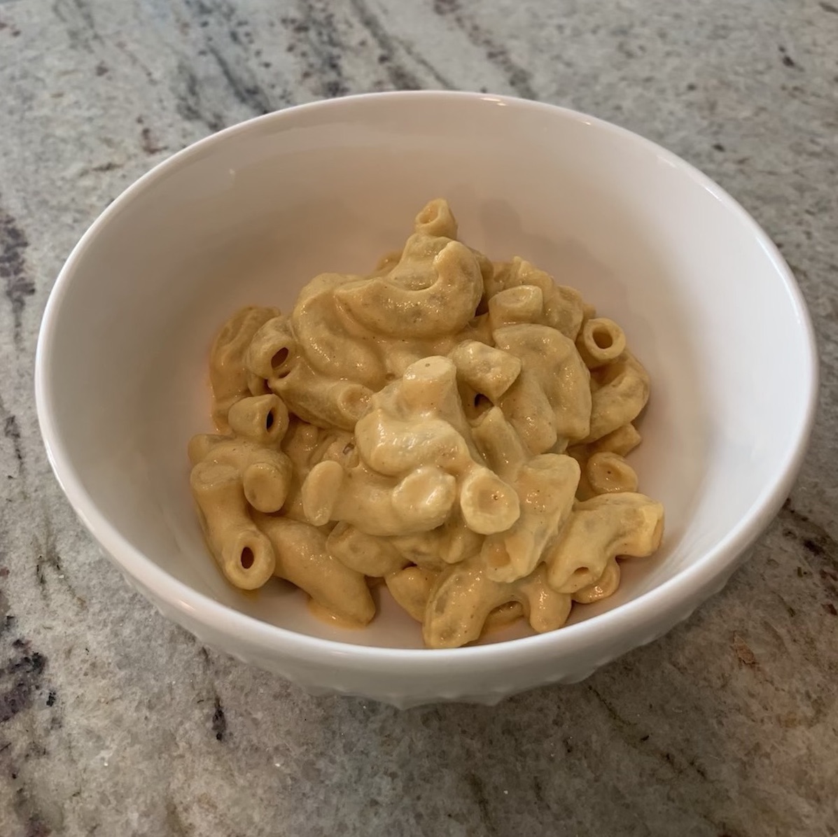 vegan mac and cheese in a white bowl on a gray counter