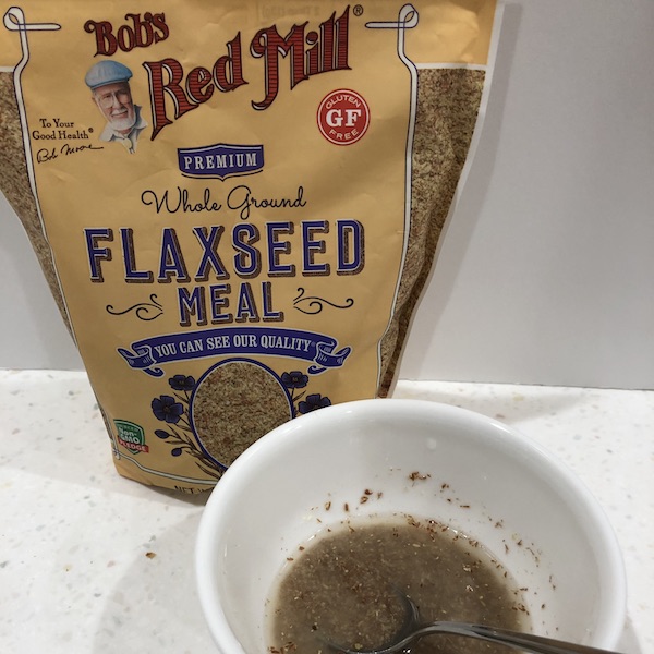 bag of ground flaxseed behind white bowl with flax egg inside