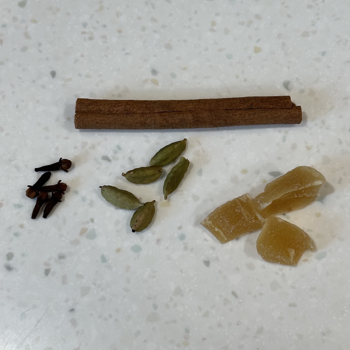 cinnamon stick with cloves, cardamom pods, and ginger below it.