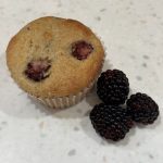 gluten free blackberry muffin on a white counter with 3 blackberries to the right.