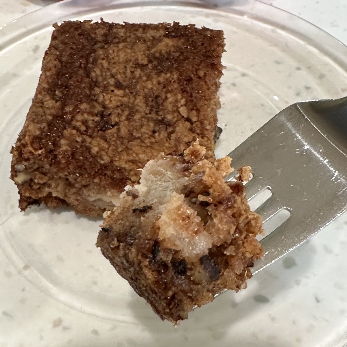 piece of apple cake on a glass plate with a bite on a fork coming toward you