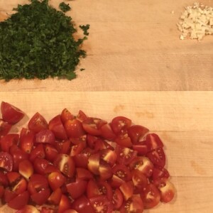 chopped tomatoes, parsley and garlic on wooden cutting board