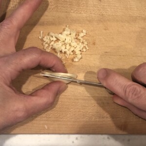 slicing garlic to mince on cutting board