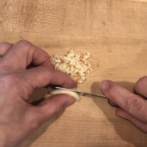 mincing garlic on a wooden cutting board