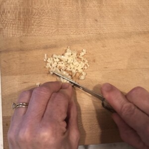 finishing mincing garlic on a wooden cutting board