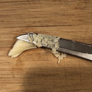 Chopping garlic with paring knife on a wooden cutting board.
